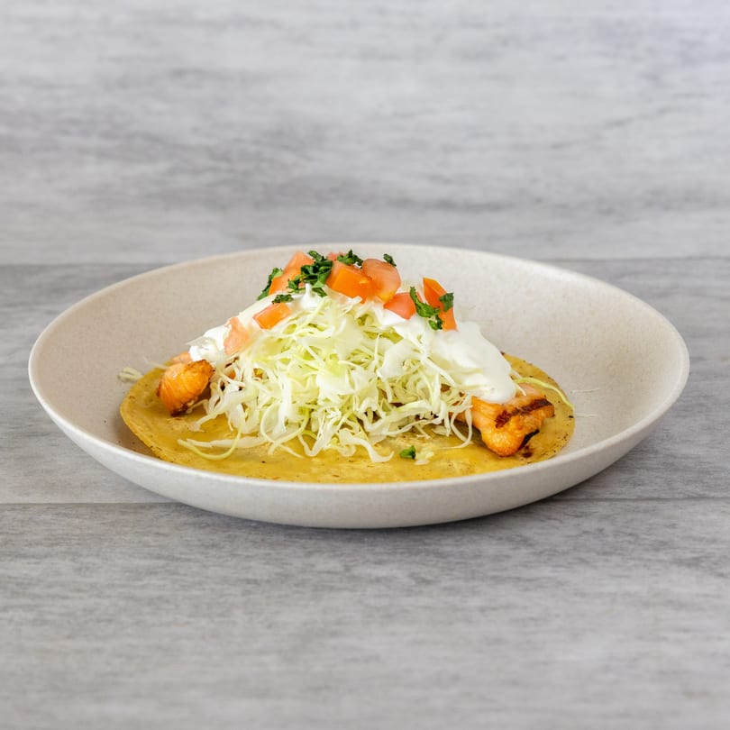 Seafood taco with grilled shrimp, shredded cabbage, diced tomatoes, and white sauce on a plate.