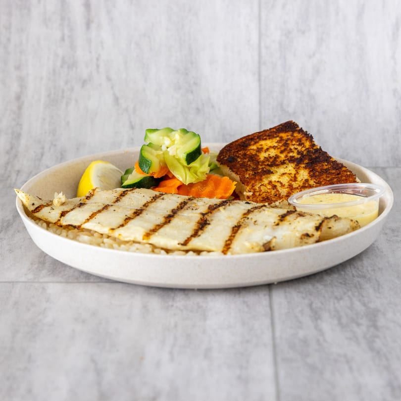 Grilled fish fillet with rice, mixed vegetables, lemon, garlic bread, and dipping sauce.